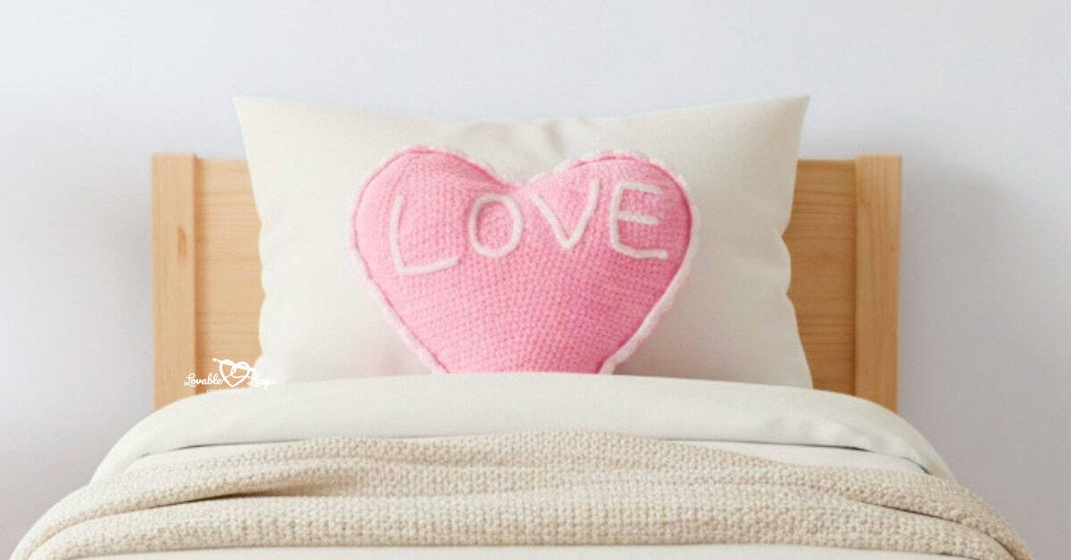 Pink crochet conversation heart pillow with &ldquo;LOVE&rdquo; propped on a pine toddler bed with white bedding.