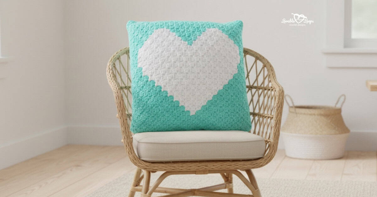 Aqua crochet heart pillow displayed on a wicker chair in a bright neutral room.