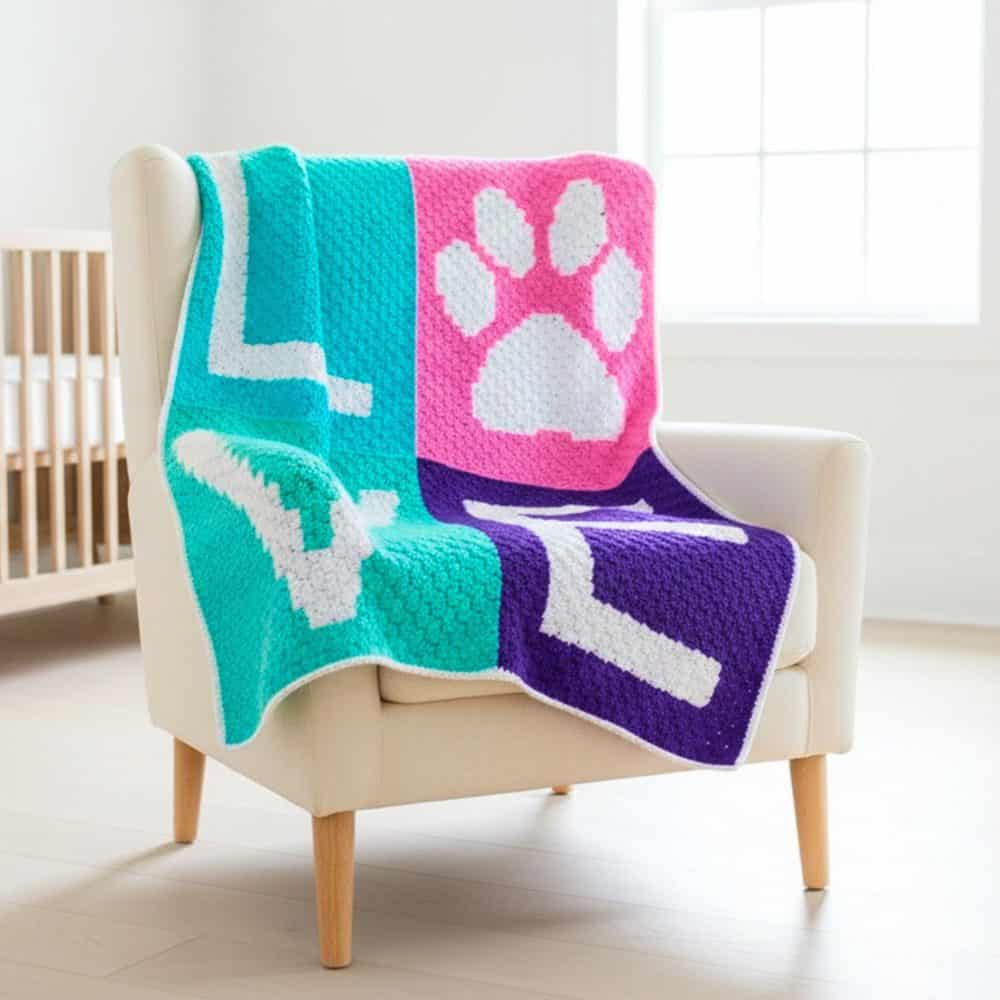 C2C love paw print crochet blanket draped over a cream armchair, featuring bold teal, pink, purple, and white blocks with the word &ldquo;LOVE&rdquo; and a paw print design.
