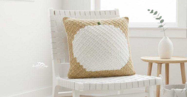Beige crochet pumpkin pillow on a white woven chair beside a small wood side table.