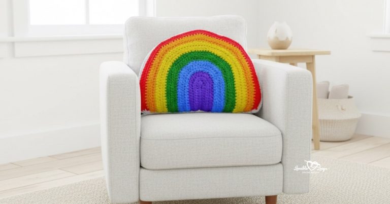 Rainbow crochet pillow centered on a white armchair in a bright neutral room.