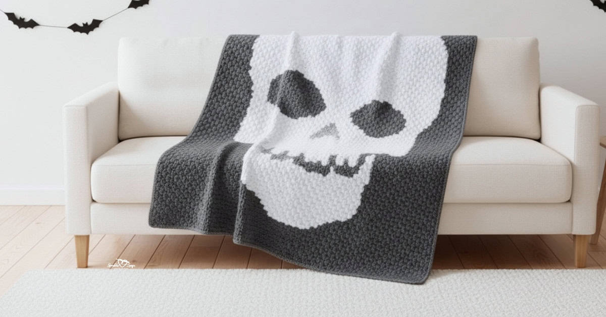 Gray crochet skull blanket draped over a cream sofa in a bright neutral living room with light wood floors, a white rug, and simple Halloween bat garland decor.