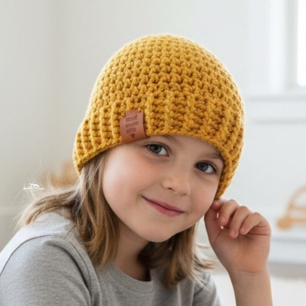 Girl wearing a mustard yellow crochet beanie with a folded brim in a bright neutral room.