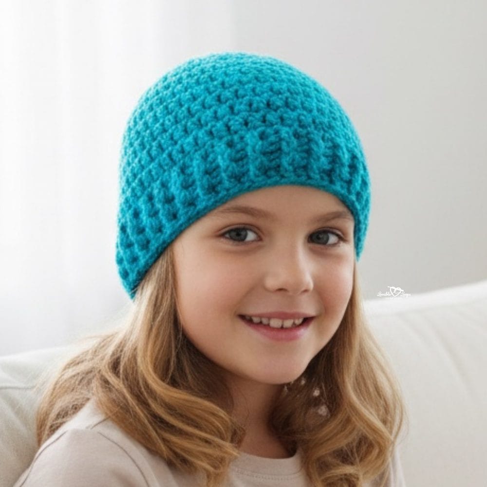 Girl wearing a teal crochet beanie while sitting on a white couch in a bright neutral room.