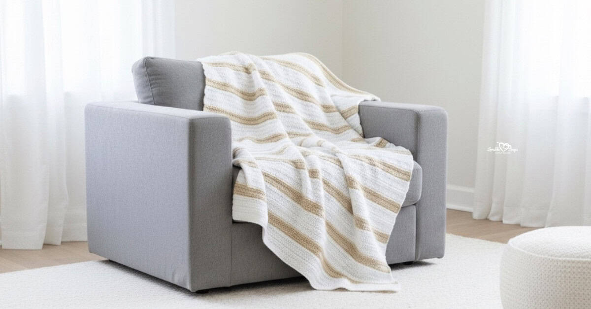 Neutral striped double crochet blanket draped over a gray armchair in a bright, minimalist room with soft white curtains