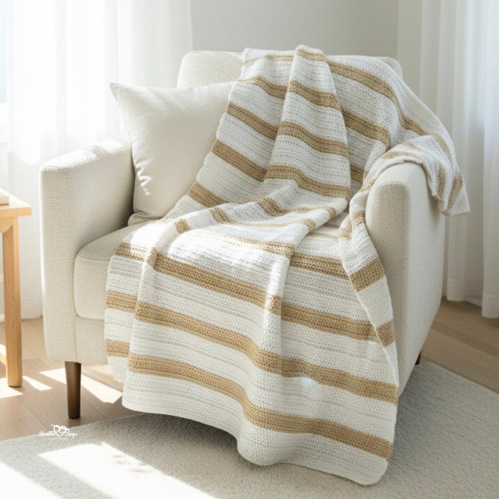 Neutral striped double crochet blanket draped over a cream armchair in a bright room with soft curtains and natural light