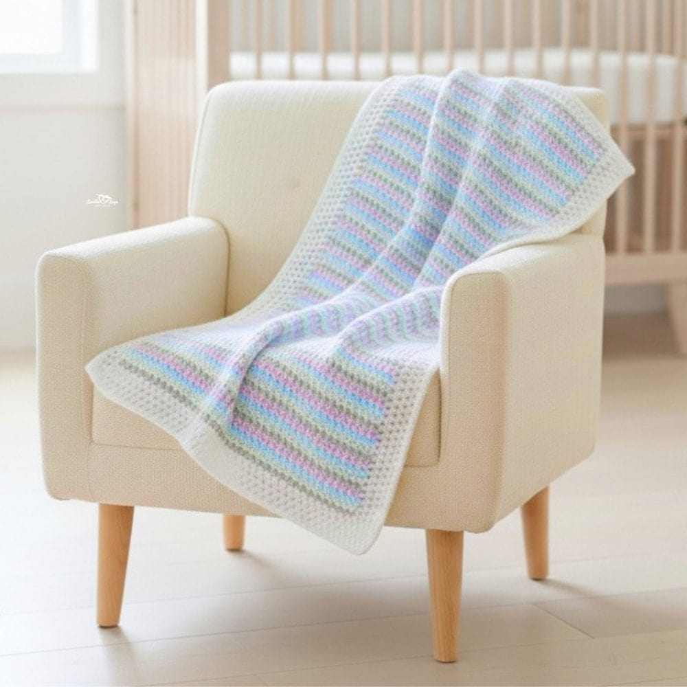 Pastel striped moss stitch crochet baby blanket draped over a cream armchair in a nursery.