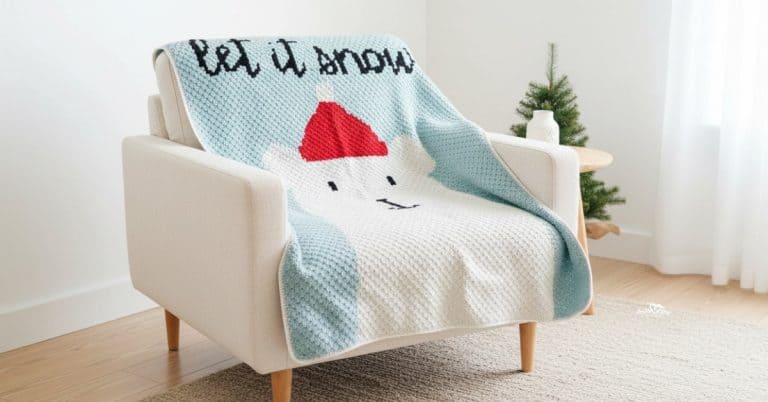 C2C polar bear crochet blanket with a polar bear face, red winter hat, and &ldquo;Let it snow&rdquo; text draped over a cream armchair in a bright living room with subtle Christmas decor.