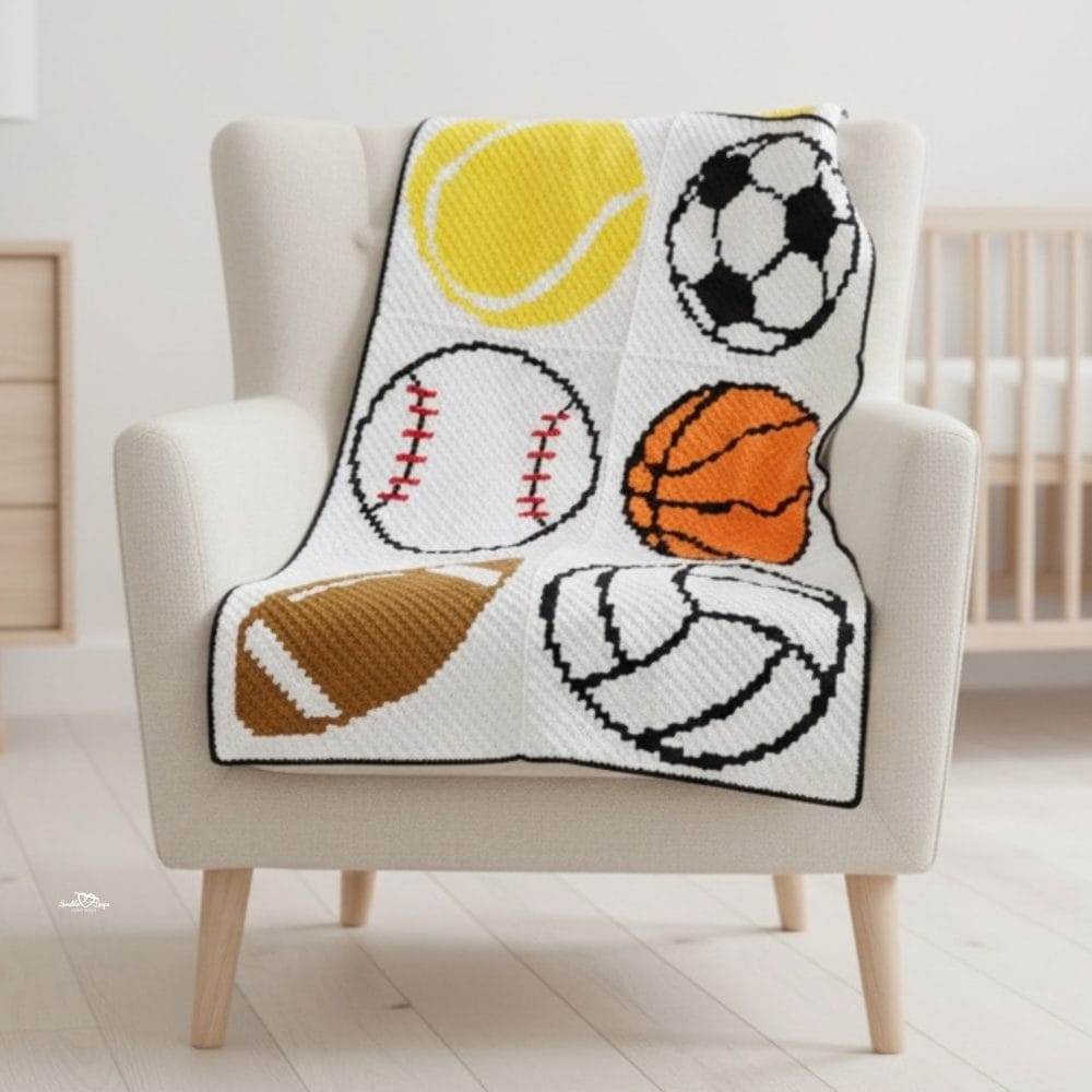 C2C sports crochet blanket draped over a cream armchair, featuring a tennis ball, soccer ball, baseball, basketball, football, and volleyball.