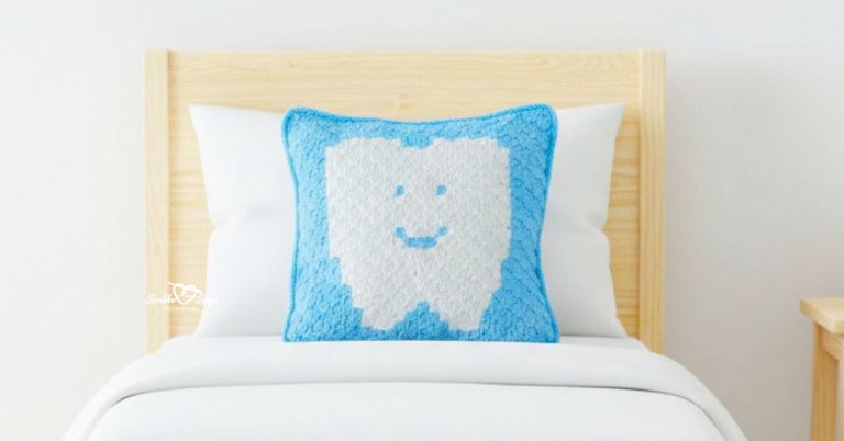 Blue tooth fairy crochet pillow propped on a pine toddler bed with white bedding.