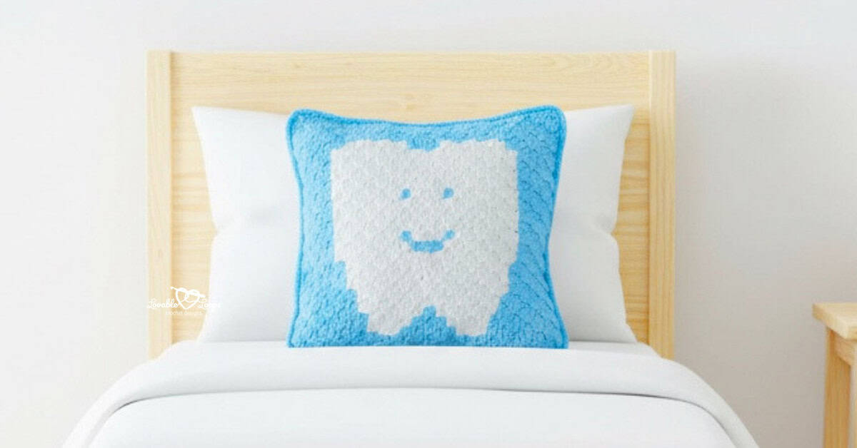 Blue tooth fairy crochet pillow propped on a pine toddler bed with white bedding.