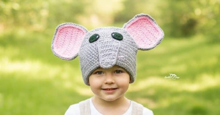Child wearing a gray crochet elephant hat on a bright green nature trail with soft trees in the background