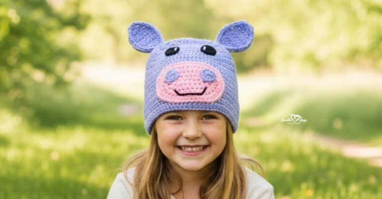 Child wearing a purple crochet hippo hat on a bright green nature trail with soft trees and a grassy path in the background