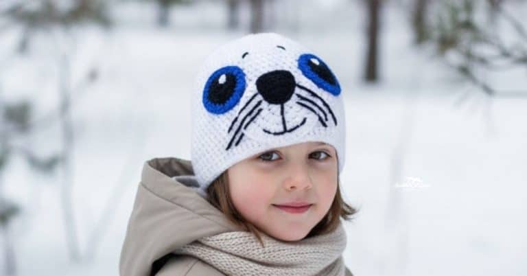 Child wearing a white crochet seal hat in a snowy winter scene with softly blurred trees in the background