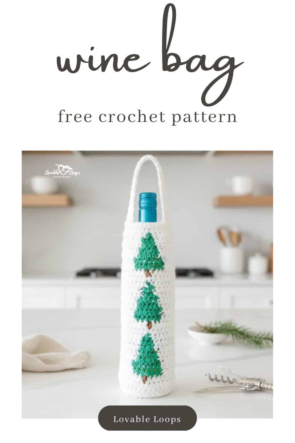 White crochet wine bottle bag with green Christmas tree motifs standing on a white kitchen island with a cream napkin, corkscrew, and small bowl with a pine sprig in a bright modern kitchen.