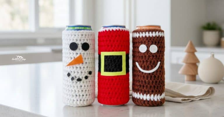 Three crochet Christmas can koozies on a white kitchen island, featuring snowman, Santa, and gingerbread designs in a bright modern kitchen with simple holiday decor.
