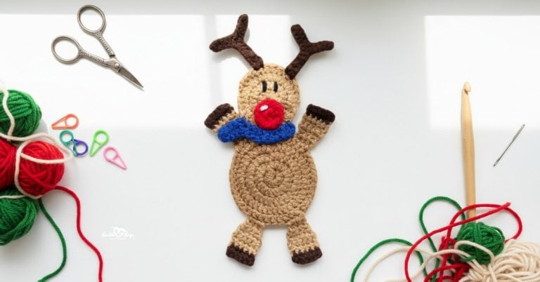 Crochet reindeer applique centered on a white desktop with scissors, a crochet hook, red and green yarn, a yarn needle, and colorful stitch markers around the edges.