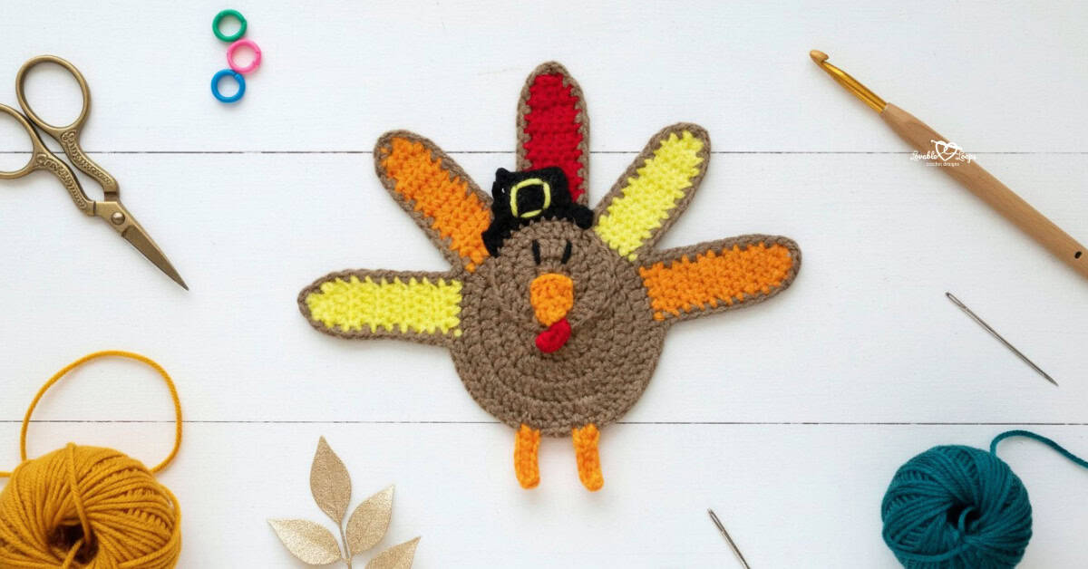 Crochet turkey applique centered on a white wooden background with scissors, a crochet hook, yarn, a yarn needle, stitch markers, and fall-inspired decor nearby.