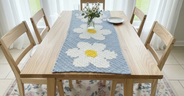 Crochet daisy table runner with large white daisies and yellow centers displayed on a light wood dining table with chairs and a vase of fresh flowers.