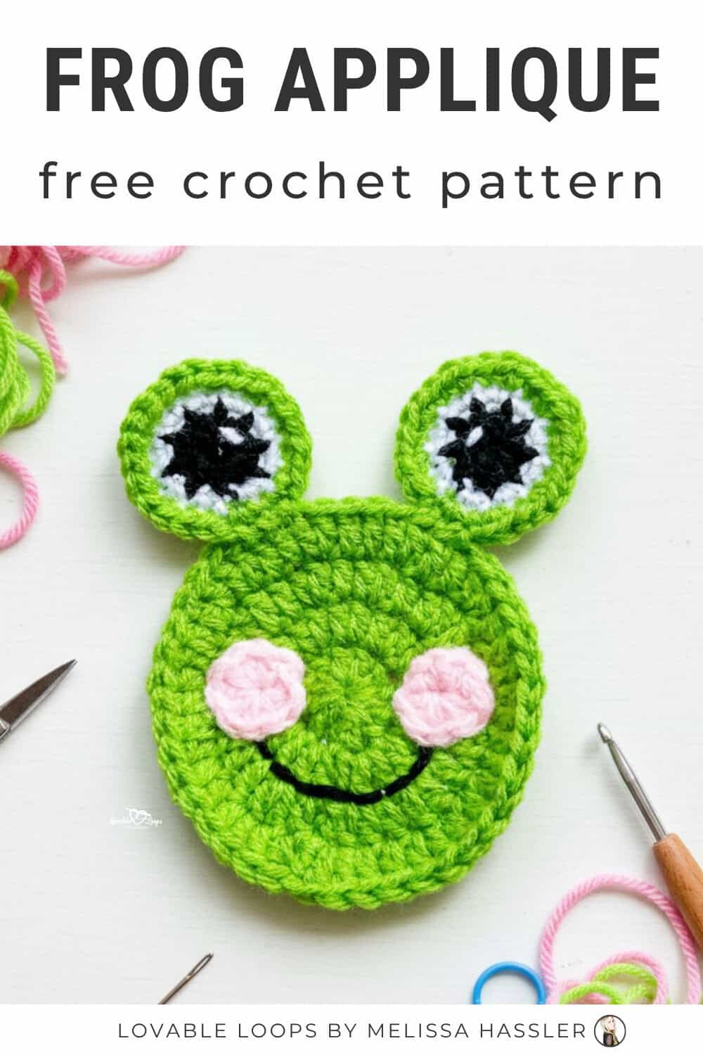 Crochet frog applique pattern on a white desktop with pink and green yarn, scissors, a crochet hook, and colorful stitch markers nearby.