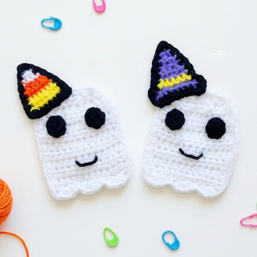Two white crochet ghost appliques with black eyes and smiling faces, one topped with a candy corn hat and the other with a purple witch hat, on a white background.