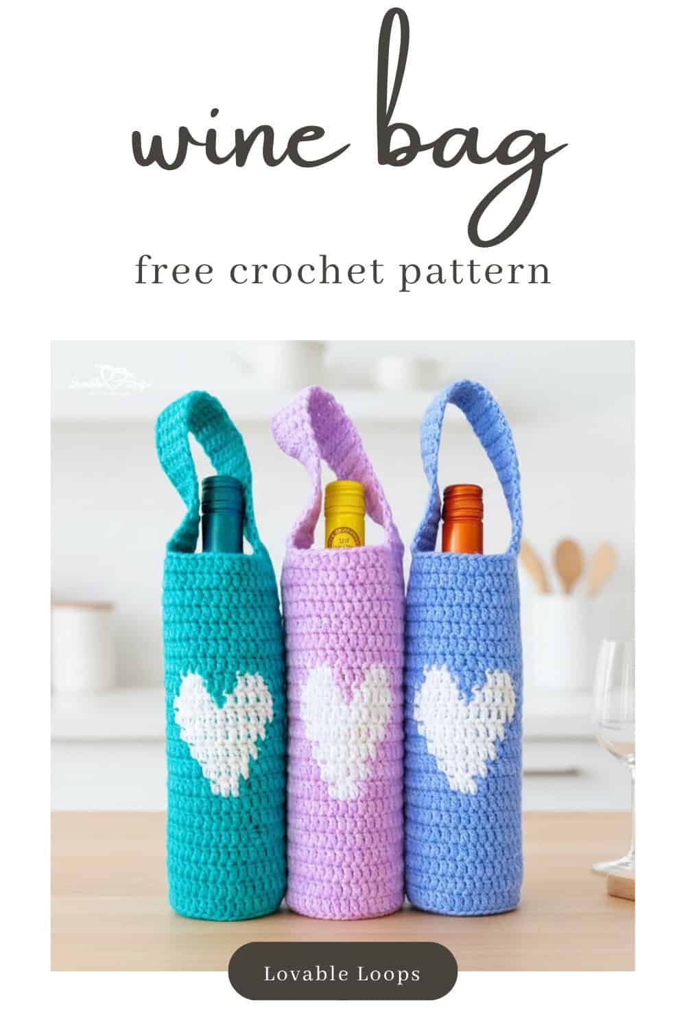 Three crochet wine bottle bags in teal, lavender, and blue with white heart motifs standing together on a light wood kitchen island in a bright modern kitchen.