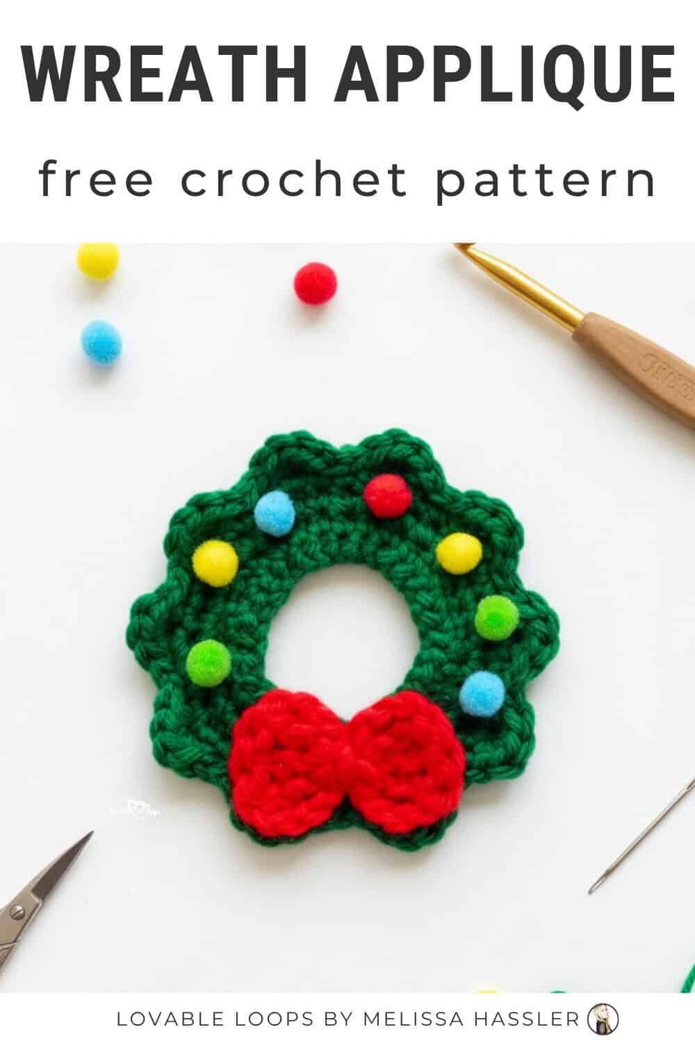 Crochet wreath applique pattern with a green wreath, red bow, and colorful pom-pom details on a white desktop with scissors, a crochet hook, and a yarn needle nearby.