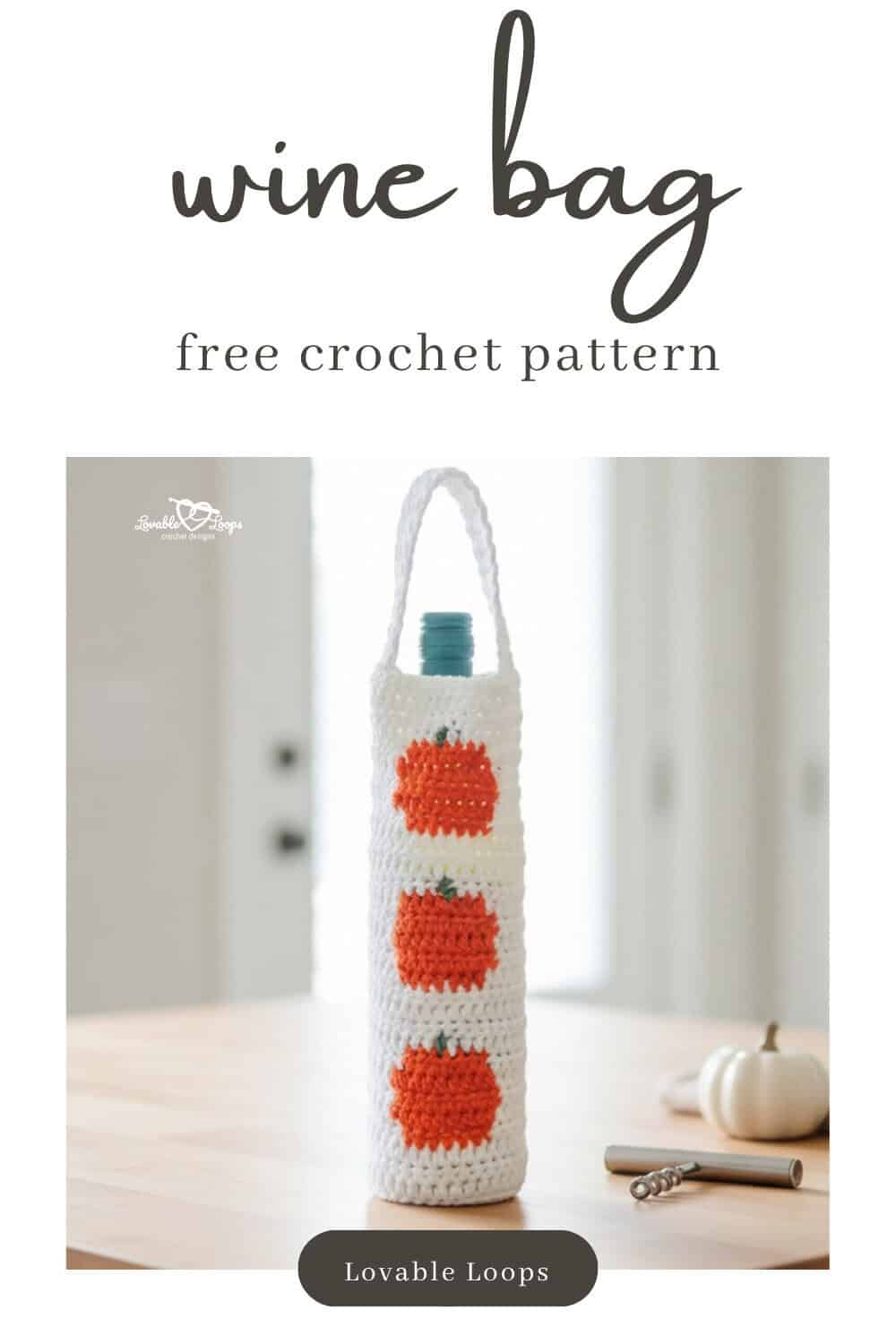 White crochet wine bottle bag with orange pumpkin motifs standing on a light wood kitchen island beside a small white pumpkin and a corkscrew in a bright kitchen.