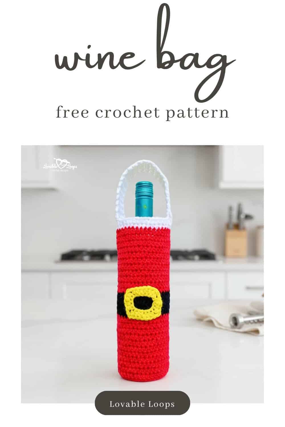 Red and white Santa crochet wine bottle bag standing on a white kitchen island with a folded cream napkin, corkscrew, and small wooden trees in a bright modern kitchen.