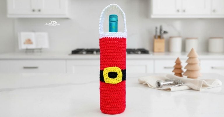 Red and white crochet Santa wine bottle bag displayed on a bright kitchen island with minimal Christmas decor in a modern white kitchen.