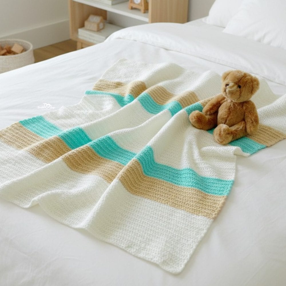 Neutral striped crochet baby blanket softly draped across a white bed in a bright kids room with a teddy bear on top.