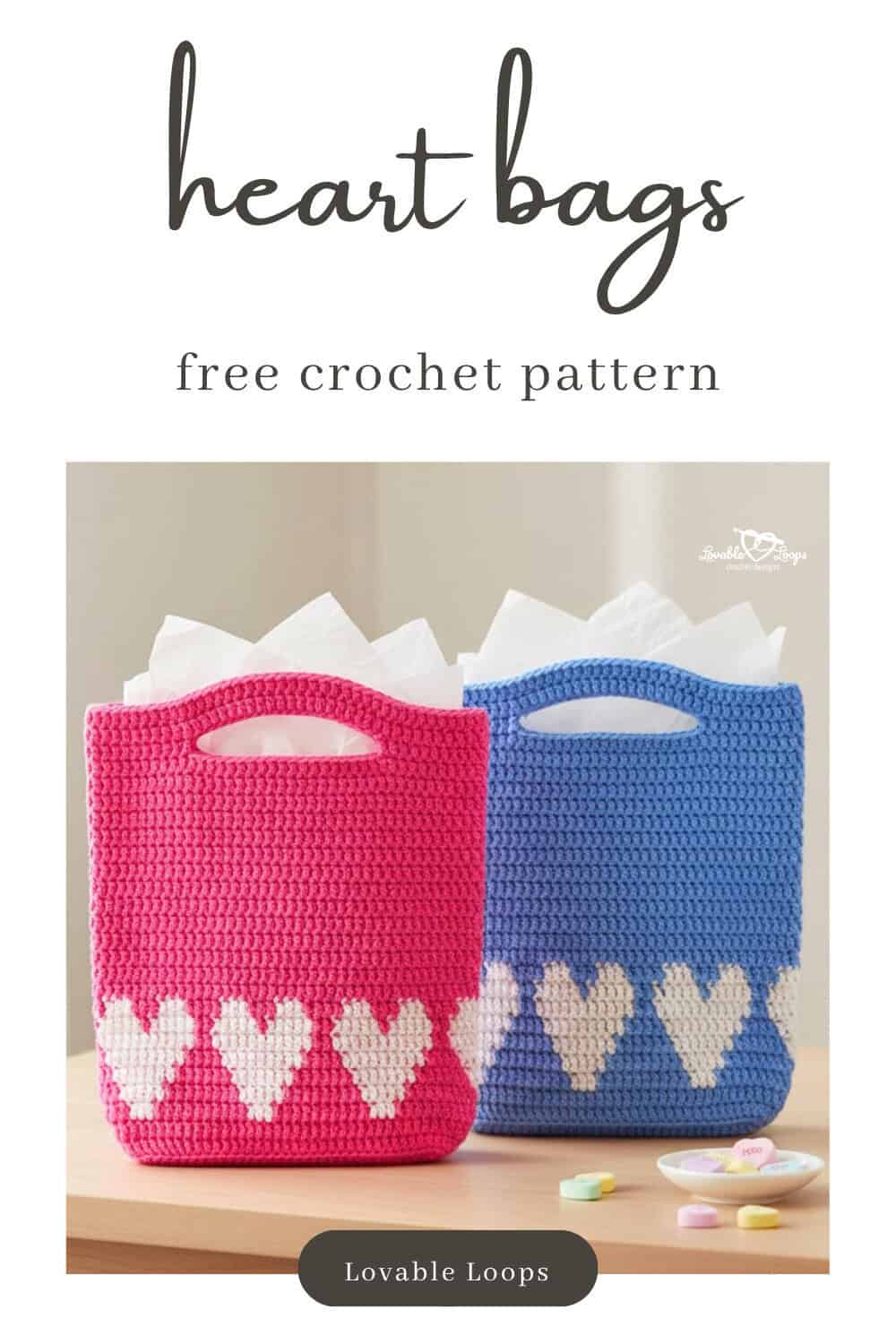 Two crochet heart gift bags on a light wood table, one pink and one blue, both filled with white tissue paper and finished with white heart designs across the lower half.