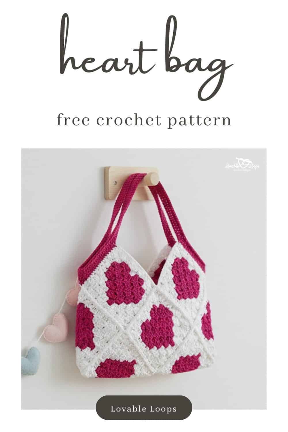 White crochet heart bag with pink C2C heart squares hanging from a wooden wall hook in a bright room, styled with a soft pastel heart garland nearby.