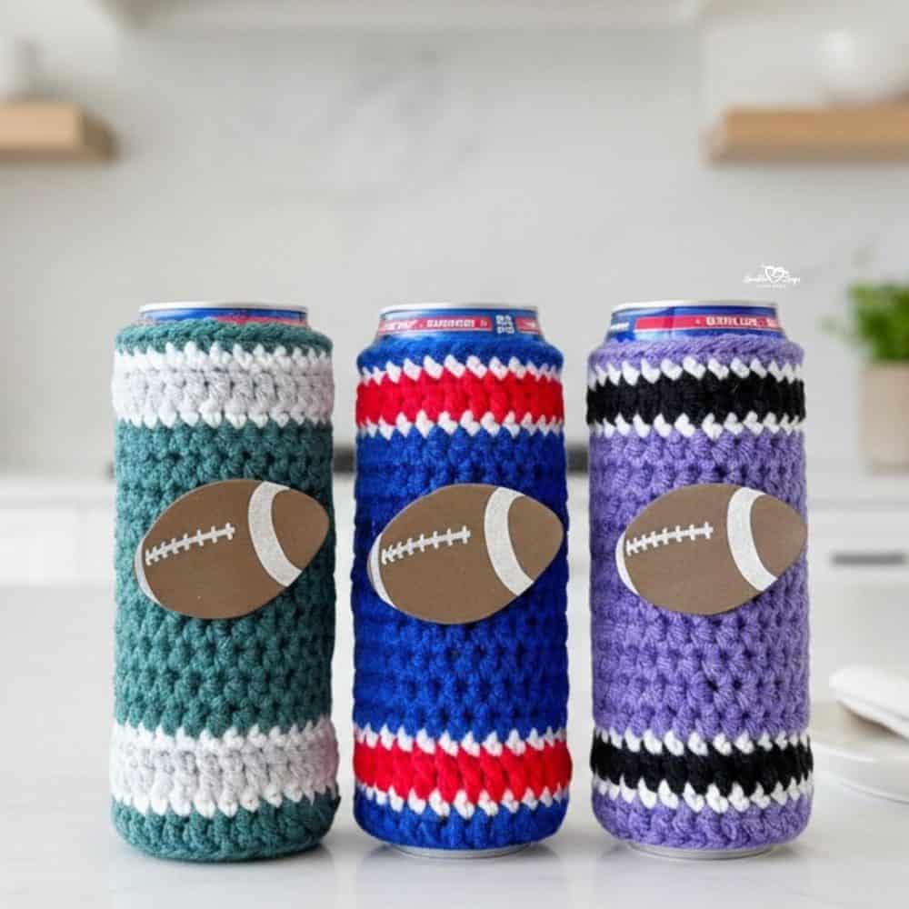 Football-themed crochet can cozies displayed on a bright kitchen island, featuring teal, royal blue, and lavender striped designs with football details in a clean modern kitchen.