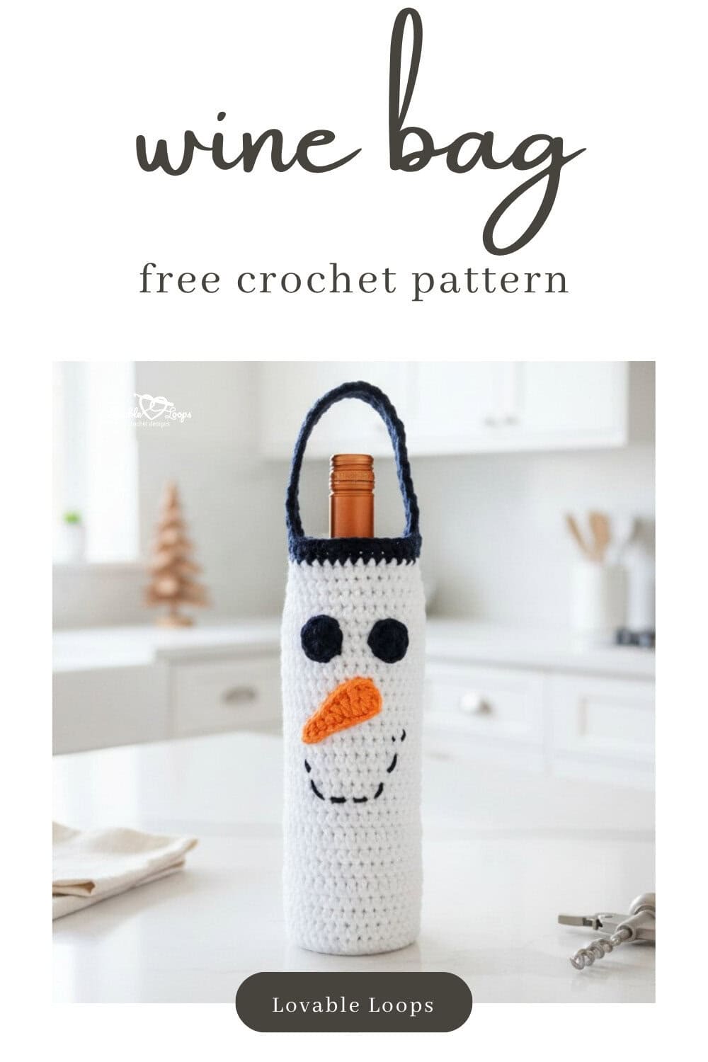 White crochet snowman wine bottle bag standing on a white kitchen island with a cream napkin, corkscrew, and small wooden trees in a bright modern kitchen.