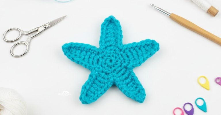 Crochet starfish applique pattern in bright turquoise yarn on a white desktop with scissors, crochet hook, yarn, and colorful stitch markers nearby.