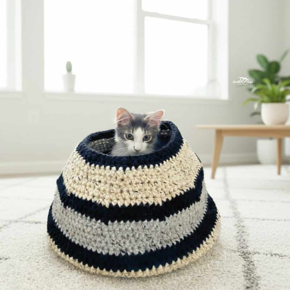 Gray and white cat peeking out of a striped crochet cat basket on a white rug in a bright modern living room.