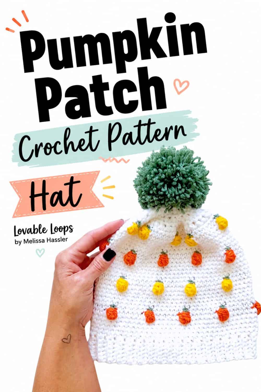 Pumpkin patch crochet hat pattern pin featuring a white beanie decorated with small orange and yellow pumpkins, green stems, and a large sage green pom-pom, held by a hand with black nail polish.
