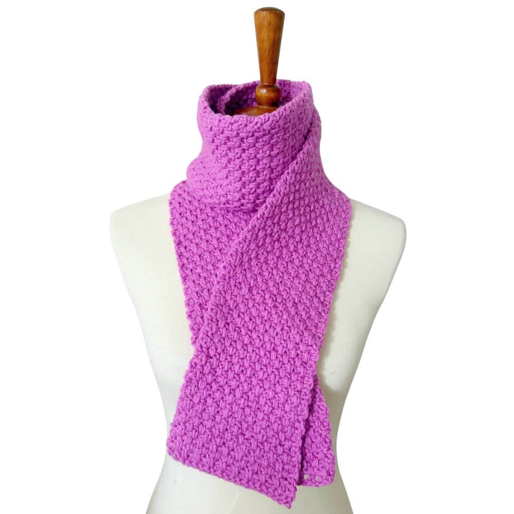 Pink crochet moss stitch scarf draped around a dress form, showing the finished scarf and textured stitch pattern.